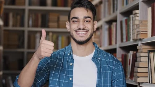 Closeup Happy Young Hispanic Guy Student Standing in Public University Library Smiling Showing Thumb