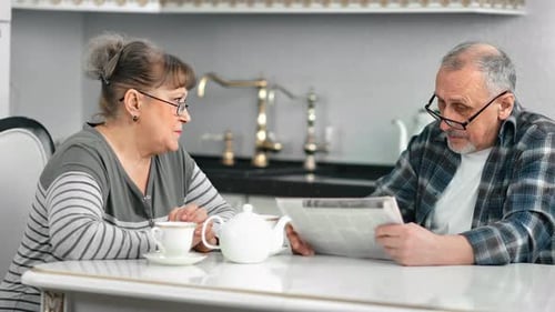 Middle Aged Mature Couple Talking Debating During Breakfast at White Kitchen Medium Shot