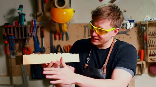 Portrait of Handsome Carpenter Working with Plank in Workshop Blowing a Dust