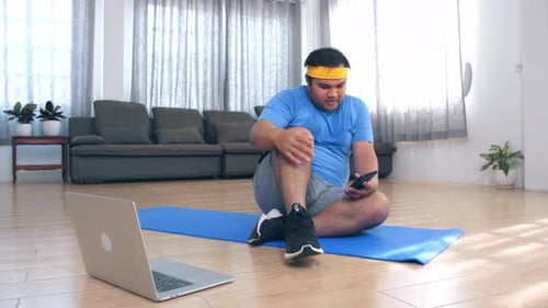 Man Sits on Exercise Mat Using Phone