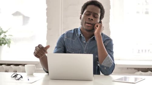 Young Adult Talking on Mobile Phone at Desk