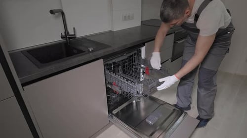 Ein professioneller Mechaniker in Overalls überprüft einen Haushaltsgeschirrspüler in der Küche