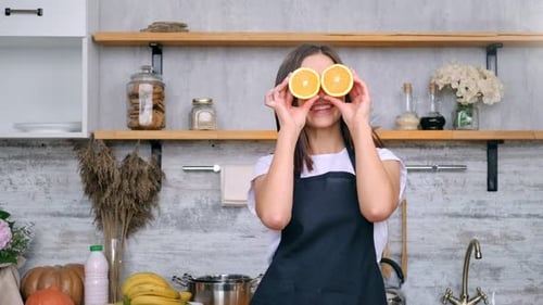 Smiling Woman with Oranges in a Sunny Kitchen