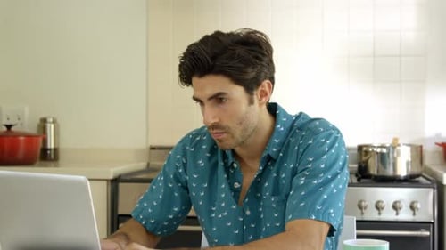 Young Man Working on Laptop in Bright Kitchen