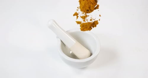 Currypulver fällt in einen Mörser und Stößel vor weißem Hintergrund, Zeitlupe 4K