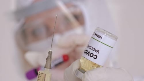 Doctor in a Medical Protective Suit Holding a Coronavirus Vaccine and a Syringe