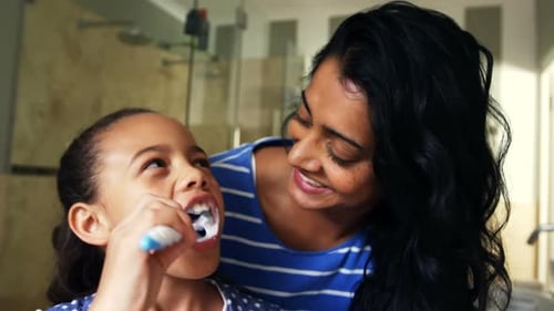 Child Brushing Teeth Watched by Smiling Woman