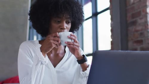 Happy african american woman sitting in cafe drinking cup of coffee and smiling