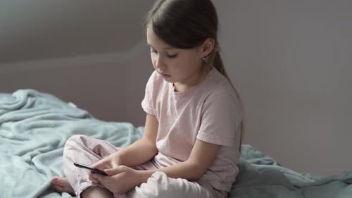 Girl Sits on Bed Looking at Phone