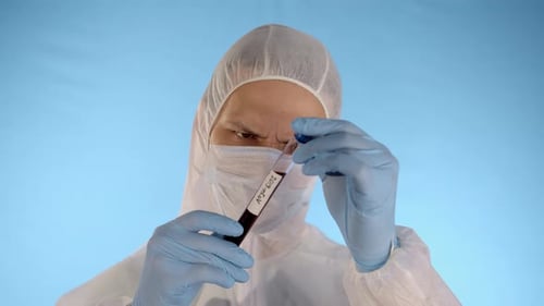 Hombre con traje protector, máscara, guantes, sostiene y deja caer el tubo de ensayo con coronavirus
