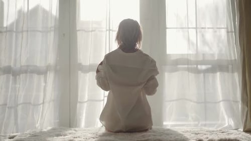Rückansicht eines jungen kaukasischen Mädchens, das morgens auf dem Bett sitzt. Blonde Charmante Frau beim Aufwachen