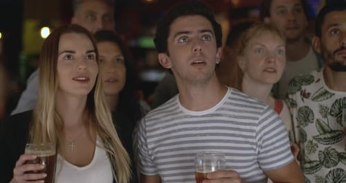 Sports fans cheering while watching televised match in sports bar, slow motion