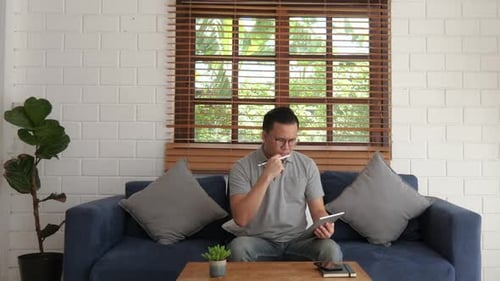 Man Sitting on Sofa Using Tablet With Stylus