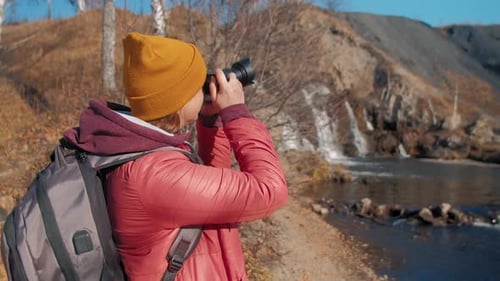 Une femme photographie un paysage d'automne avec une rivière