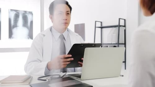 Asia male doctor great news talk symptoms with female patient sitting at desk in health clinic.