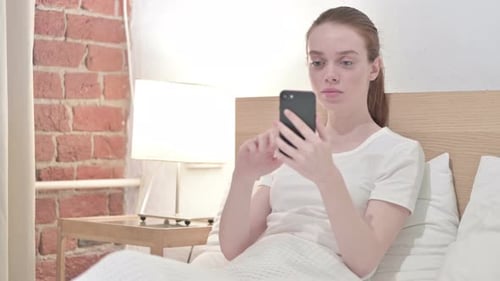 Young Woman Using Phone in Bed