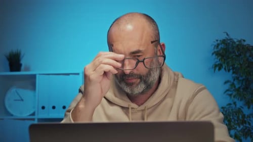 Tired Man Working at Computer Rubs Eyes