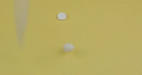 Many Pills Fall on a Yellow Surface. Round and Oval White Pills