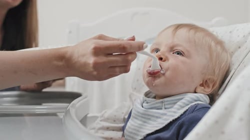 Cute Baby Being Fed with Spoon in Highchair