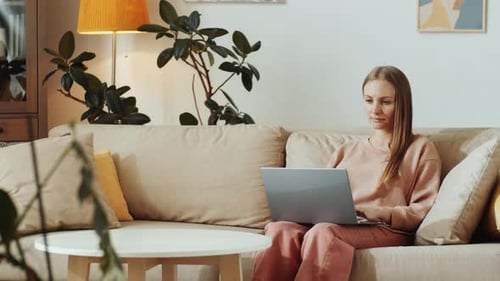 Woman Using Laptop on Sofa in Bright Home