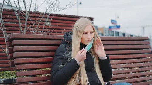 Woman Puts on Surgical Mask on Park Bench