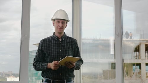 Senior engineer in hardhat swiping on tablet and looking