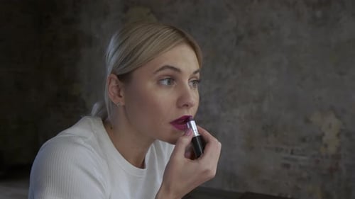 Frau malt ihre Lippen mit Lippenstift auf einem schwarzen Hintergrund, blonde junge Frau
