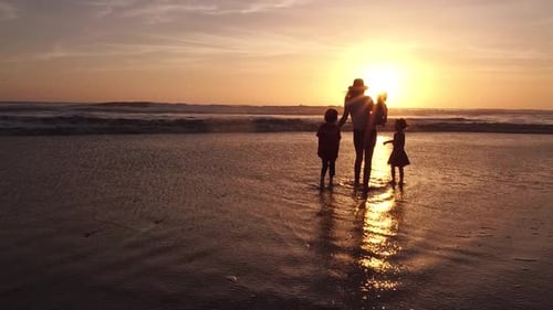 A woman enjoys a stunning and colorful sunset with her three children at the beach in slow motion.