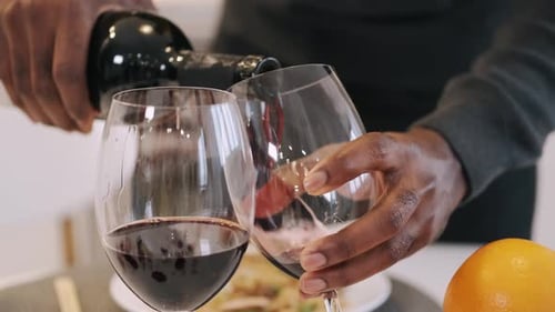 Afroamerikaner gießt Wein in Gläser für ein romantisches Abendessen