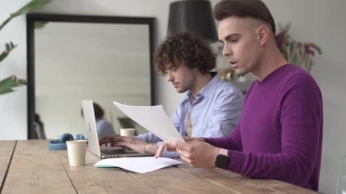 Couple homosexuel de sexe masculin travaillant, s'occupant des finances et de la paperasse à la maison, calculant le budget de la vie domestique