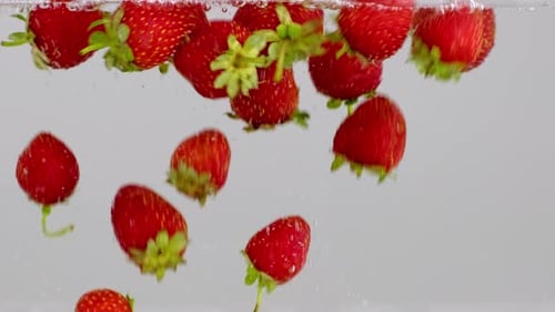 Red strawberry berry falling into transparent water on white background