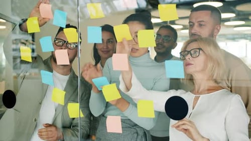 Business People Solving Business Problems in Office Using Sticky Notes on Glass Board