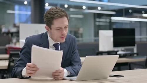 Businessman with Laptop Reading Documents in Office