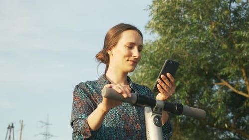 Woman Using Phone by Electric Scooter in City
