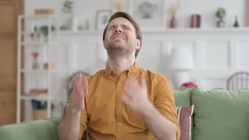 Man Crying and Raising Hands on Couch