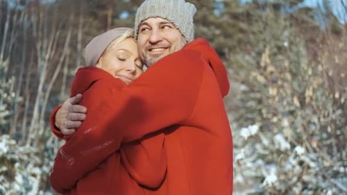 Young Happy Couple in Red Sweaters in the Winter Forest Look at Each Other and Smile