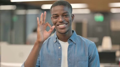 Smiling Man Gives OK Gesture in Workplace