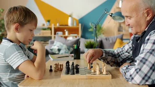 Smart Kid Playing Chess with Grandfather at Home Enjoying Indoor Game at Table