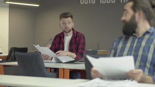 Two Colleagues Sitting in Office Studying New Working Information From Papers