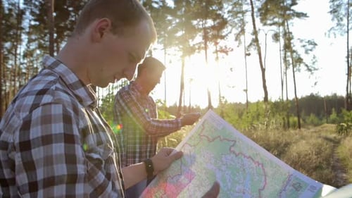Travelers with a map and a compass in their hands are looking for their way. Terrain orientation.