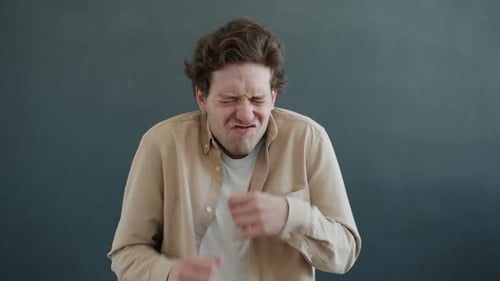 Verspielter Kerl macht lustige Grimassen und Gesten beim Blick in die Kamera auf grauem Hintergrund