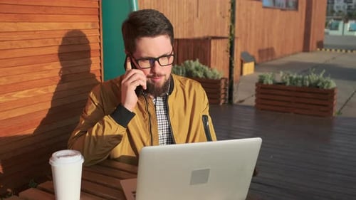 Man Works on Laptop and Talks on Phone