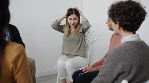 Nervous Young Woman Sharing Feelings During Group Therapy Sitting in Circle in White Room