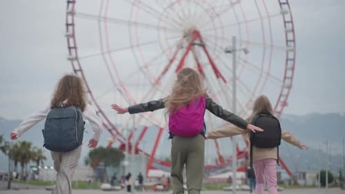 Happy School Children with Bags Run to Giant Wheel Raise Hands Imitating Flight