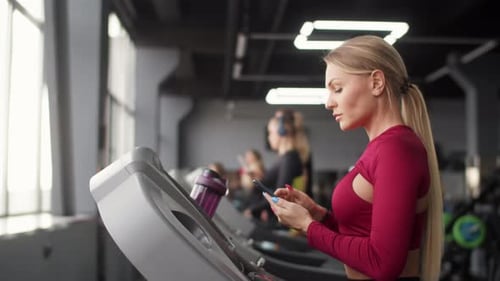 Woman Using Phone on Gym Treadmill