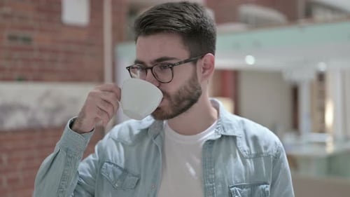 Young Man with Glasses Drinking Hot Beverage