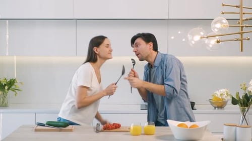 Happy Couple Singing with Utensils in Modern Kitchen