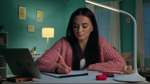 Woman Writing Notes at Desk With Laptop