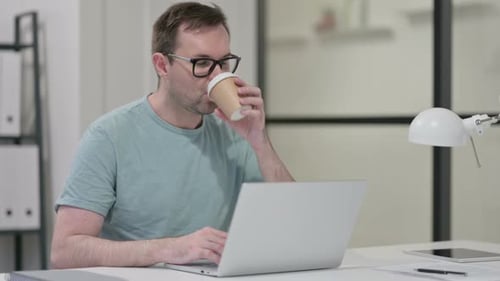 Junger Mann trinkt Kaffee beim Tippen auf Laptop