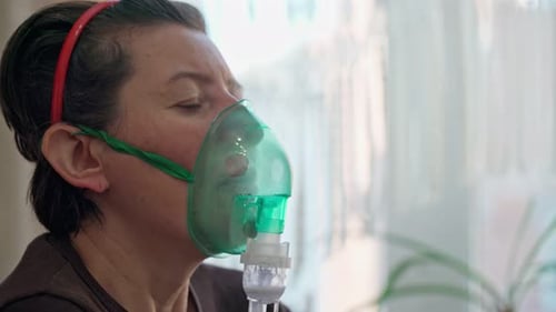 Une femme européenne à la maison effectue une inhalation de vapeurs d'huile oxygène à travers un masque